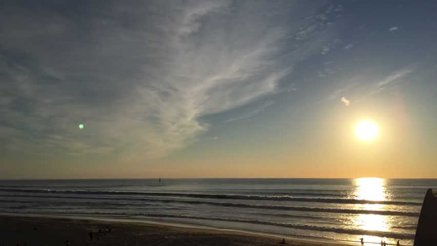 Timelapse Of Colourful Sunset Over Ocean Horizon With People Walking On The Beach, Birds Flying, Waves Rolling And Clouds Moving While The Bright Sky Colours Change Through Hues of Pink, Orange, Red