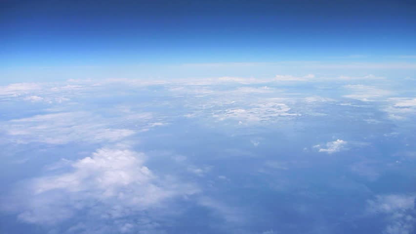 Flying in airplane over Pacific Ocean with clouds below and blue sky atmosphere,