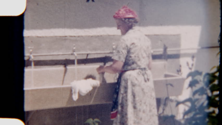 8mm footage of a mother hand-washing clothes in an outdoor sink bathed in warm morning sunlight capturing a gentle nostalgic moment of everyday routine