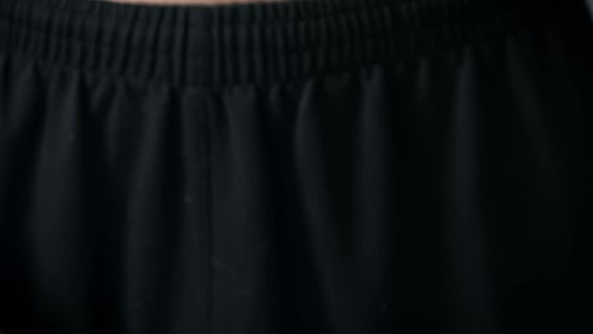 Close-up of a hand taking a flashlight from black pants and pointing its powerful bright beam directly into the camera lens, creating a dramatic blue flare effect.