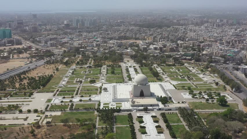 Wide-angle aerial drone footage of Mazar-e-Quaid, the mausoleum of Muhammad Ali Jinnah, with the Karachi city skyline in the background. Famous national monument and landmark of Pakistan