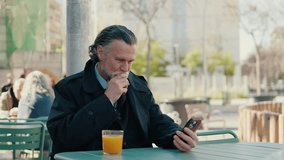 A mature businessman enjoys a glass of orange juice while using his phone at an outdoor cafe. He checks messages and scrolls through content. - Powered by Shutterstock - Get 15% off with code: PIKWIZARD15