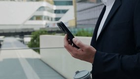 Closeup view of businessman hands holding smartphone and coffee cup in urban district. Male manager checks trade market data via mobile phone walking along street in morning - Powered by Shutterstock - Get 15% off with code: PIKWIZARD15
