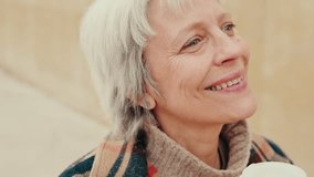 Happy senior woman drinks coffee outdoors on a cool autumn day. She's looking around and enjoying the moment. She smiles and takes a sip. - Powered by Shutterstock - Get 15% off with code: PIKWIZARD15