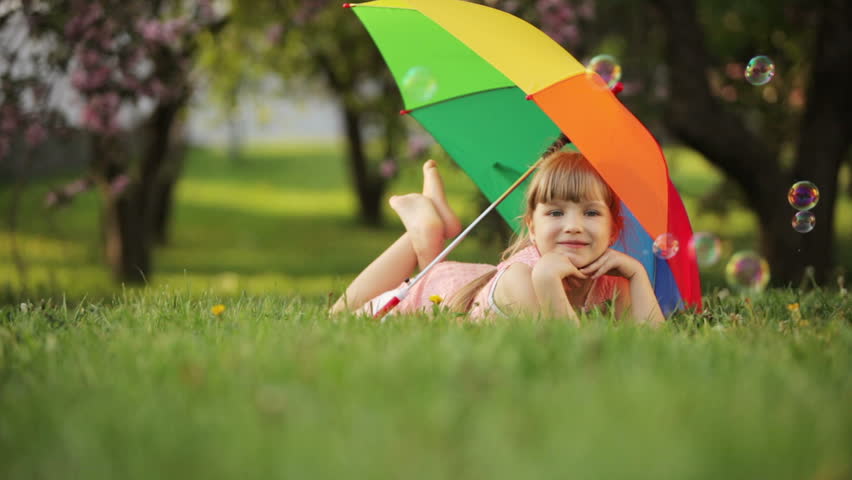 Little girl lying on grass with umbrella

