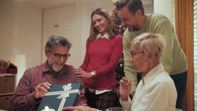 Multigenerational family members gathering near christmas tree, warmly presenting wrapped gift to delighted senior grandfather during festive holiday moment - Powered by Shutterstock - Get 15% off with code: PIKWIZARD15