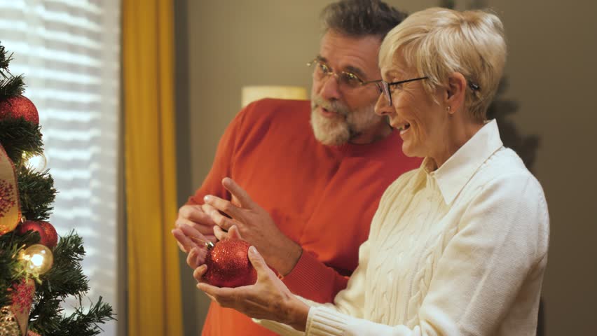 Cheerful senior couple sharing festive moment while decorating christmas tree, creating warm memories in comfortable living room setting