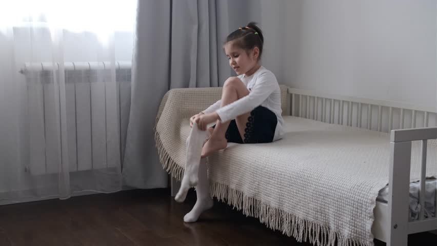 Little girl putting on tights on bed at home
