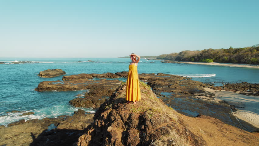 Woman in yellow dress overlooking rocky coastal beach San Juanillo in Costa Rica