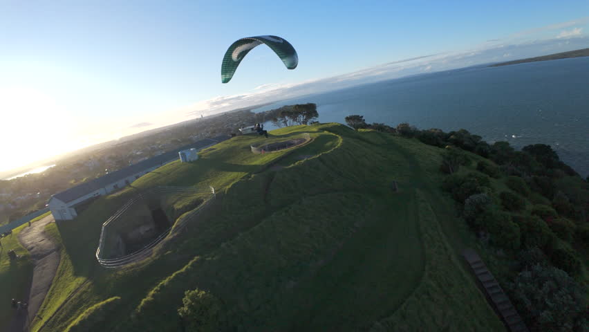 Paraglider soaring along the coastline at North Head near Auckland, New Zealand, showing aerial views of flight and landscape.
