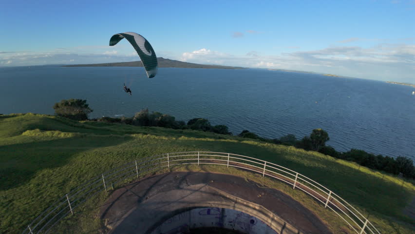 Paraglider soaring along the coastline at North Head near Auckland, New Zealand, showing aerial views of flight and landscape.