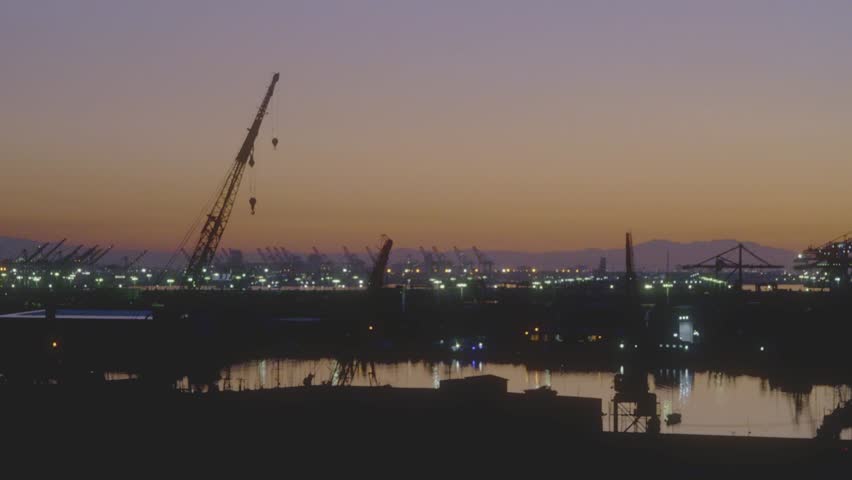 Industrial harbor scene at dusk with silhouetted cranes standing tall against a softly lit sky. Serene yet industrial atmosphere