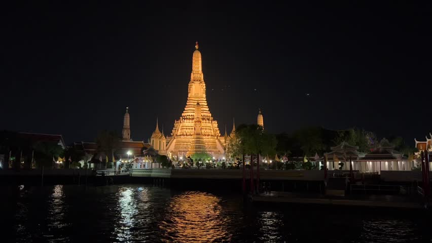 Wat Arun temple glowing at night with ornate central spire reflected in calm Chao Phraya River waters under dark serene sky, showcasing iconic Bangkok landmark in Thailand