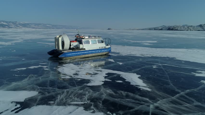 Aerial flight around Khivus, hovercraft rides on frozen winter Lake Baikal. Siberia, incredible winter journey. Picturesque cracked ice, sunny. Best tourist destinations in Russia. Mountains, horizon