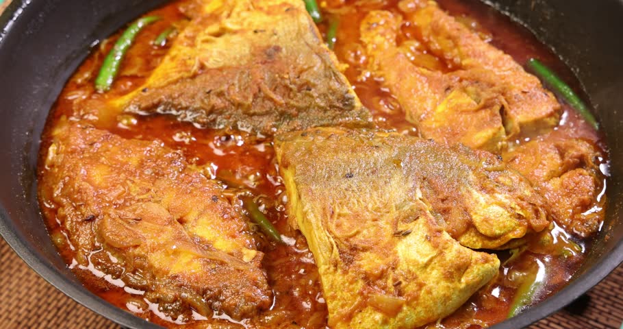Asian style hot spicy pomfret fish curry masala cooking bubbling heat steam in saucepan sprinkle coriander leaf 