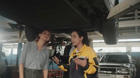 Latin mechanic manager explains to White female client and Black insured agent about EV car undercarriage fix work, claim warranty service maintenance at automotive garage, transportation industry. - Powered by Shutterstock - Get 15% off with code: PIKWIZARD15