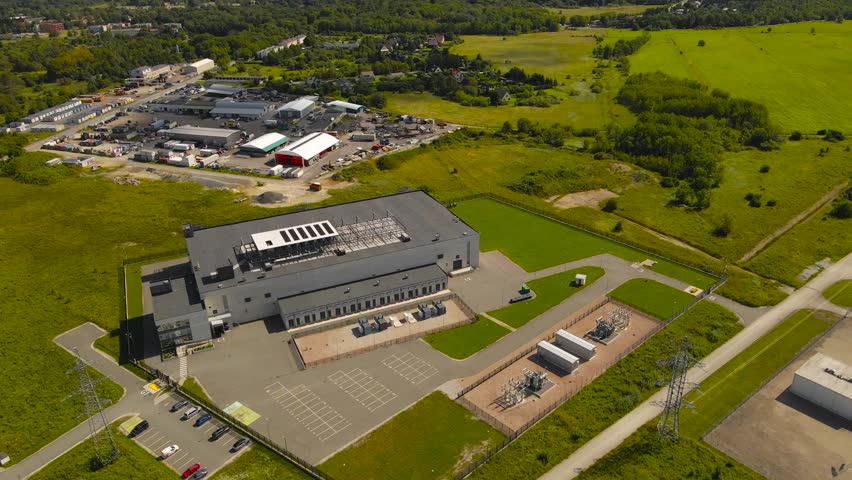 Aerial drone footage orbiting and flying around a large modern gray and white colored data center with cooling system ventilation fans on the rooftops and green grassy countryside around it, servers.