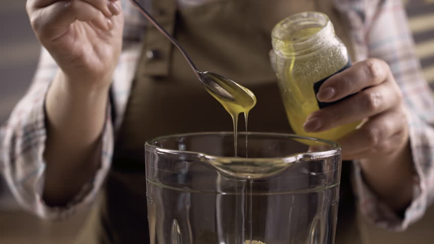 female hands pouring honey into blender glass