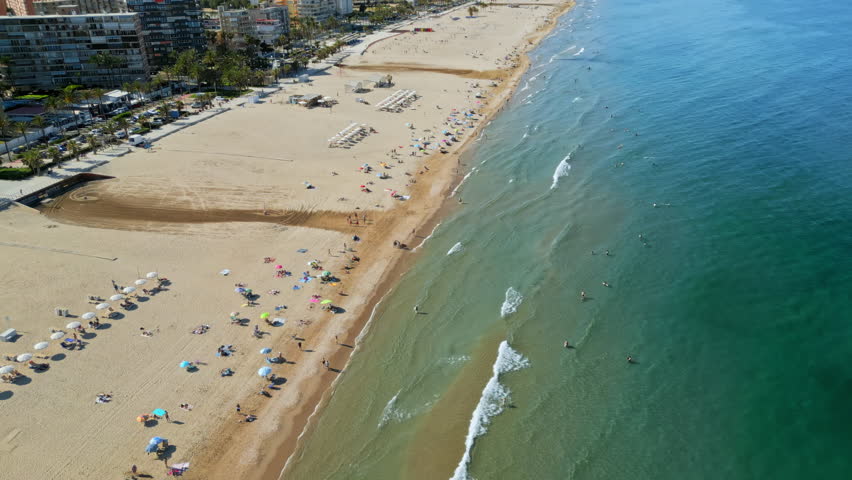 Aerial drone view of the buildings along the coastline with people relaxing on the beach in Benidorm, Spain in daylight
