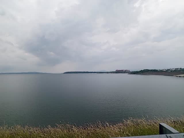 Atmospheric Moody Dark clouds loom over a still lake.A winding path is lit by solitary streetlights. Tall grasses sway in the breeze, enhancing the moody, pre storm atmosphere.

