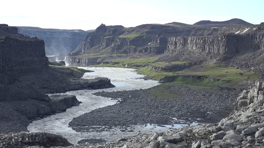 Expansive view of the rugged terrain surrounding Dettifoss waterfall, with jagged cliffs, rocky outcrops, and the river cutting through the canyon. 