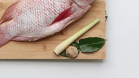 One fresh Red Tilapia fish and Galangal, lemongrass, kaffir lime leaves on a wooden board on a white background. - Powered by Shutterstock - Get 15% off with code: PIKWIZARD15