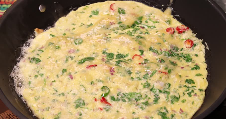 Asian Masala omelette red green chilli onion coriander leaf tomato spicy fried egg sizzling bubbling in frying pan 