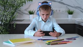  Boy wearing headphones with phone in his hands using smartphone technology while doing homework. Concept of children's dependence on mobile games. Online Education. - Powered by Shutterstock - Get 15% off with code: PIKWIZARD15