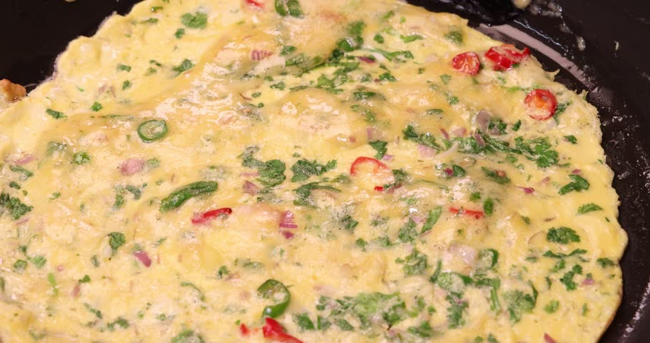 Asian Masala omelette red green chilli onion coriander leaf tomato spicy fried egg sizzling bubbling in frying pan 