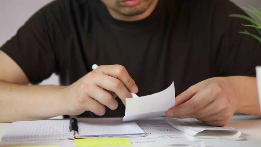 Close-up of hands scrutinizing a sales receipt and then recording details in a logbook, highlighting meticulous financial management and personal accountability.