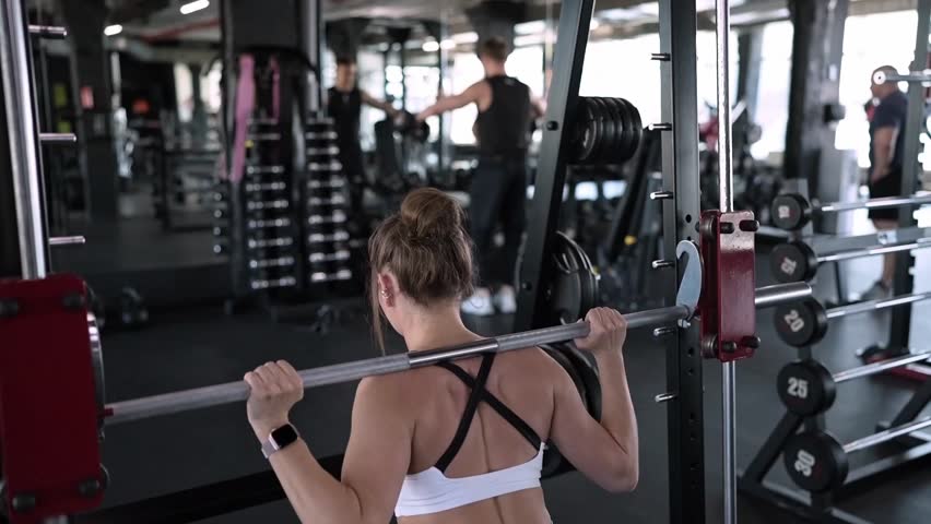 Back view, woman lifting weight, squatting with barbell in gym, sporty woman exercising 