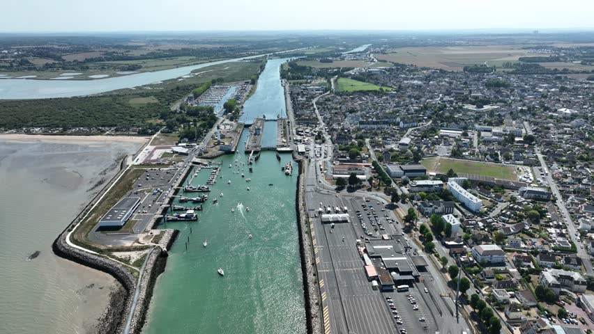 Aerial view of the canal cutting through the landscape with boats and buildings, contrasting the water with the land, Bernières-sur-Mer, Normandy, France.