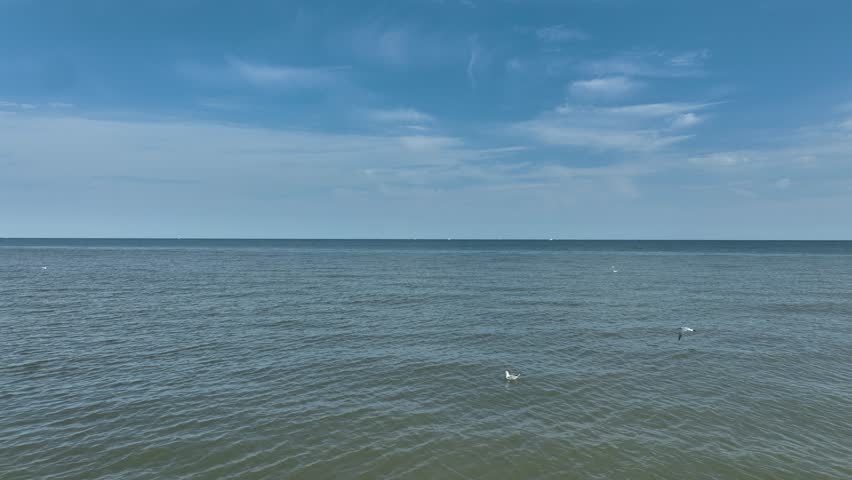 Aerial view of the vast ocean stretching to the horizon under a partly cloudy sky, showcasing the tranquil beauty of the sea, Bernières-sur-Mer, Normandy, France.