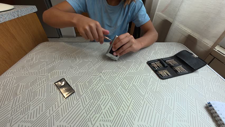 Child using precision screwdriver to repair small electronic device. Close-up of hands fixing gadget with toolkit on table, learning technical skills