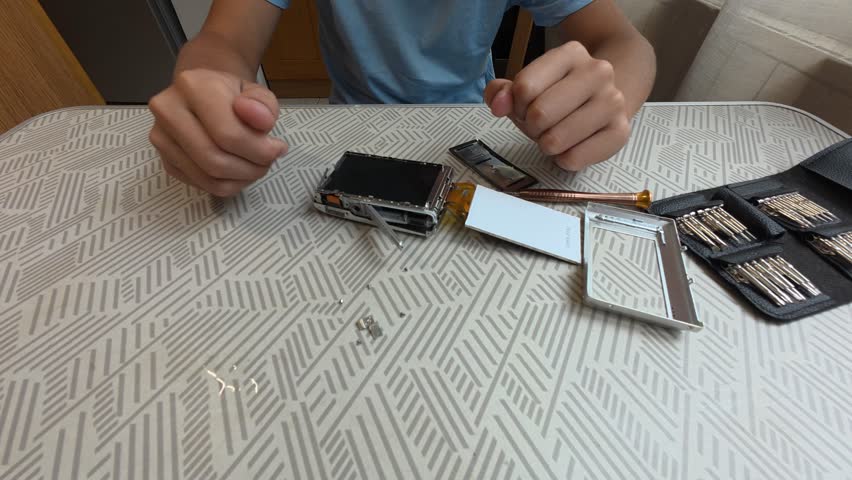 Child using precision screwdriver to repair small electronic device. Close-up of hands fixing gadget with toolkit on table, learning technical skills