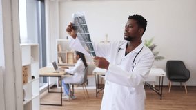 Male doctor examining x-ray images in modern office setting, female colleague working in background. Professional healthcare worker involved in radiology analysis and diagnostics. - Powered by Shutterstock - Get 15% off with code: PIKWIZARD15