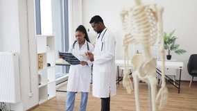 Medical professionals male and female discussing X-rays in modern clinic with skeleton model emphasizing anatomy and collaboration in medical settings - Powered by Shutterstock - Get 15% off with code: PIKWIZARD15