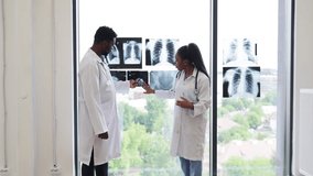 Medical professionals, male and female, reviewing x-ray diagnoses near a bright clinic window. Collaborative discussion over radiological findings indicates teamwork for accurate analysis. - Powered by Shutterstock - Get 15% off with code: PIKWIZARD15