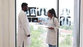 Male and female doctors of diverse backgrounds examining chest X-ray images by window. Collaborative medical consultation in modern clinic setting, emphasizing teamwork, analysis - Powered by Shutterstock - Get 15% off with code: PIKWIZARD15