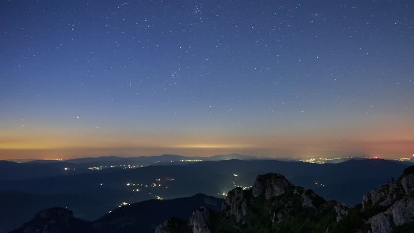 Timelapse of bright star trails over a mountain landscape illuminated by the moon