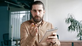 Webcam view. Businessman watching video call conference takes notes in notebook looking at camera sitting at workplace in business office. Worker listening to online training, communicates remotely - Powered by Shutterstock - Get 15% off with code: PIKWIZARD15
