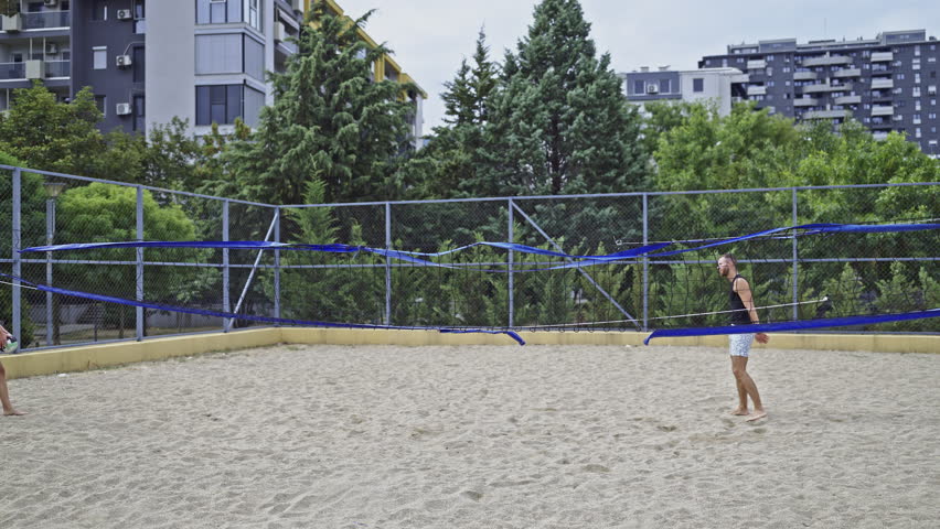 Young friends enjoys a lively game of beach volleyball on a sunny day in an urban park. They are active, having fun, and spending quality time together, showcasing friendship and outdoor recreation.