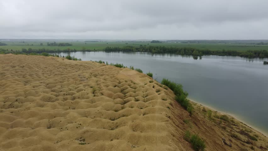 A drone shot of textured golden cliffs overlooking a calm reflective lake under clouds