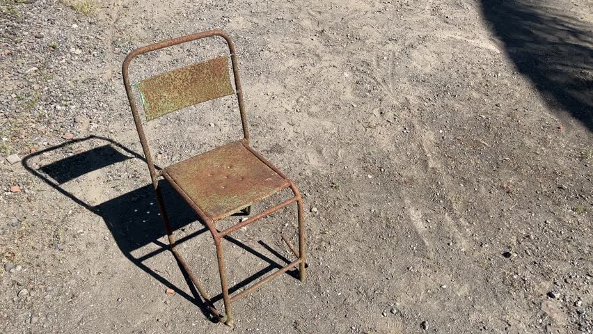 Rusty old metal chair standing outdoors, showing texture of decay and industrial aging.