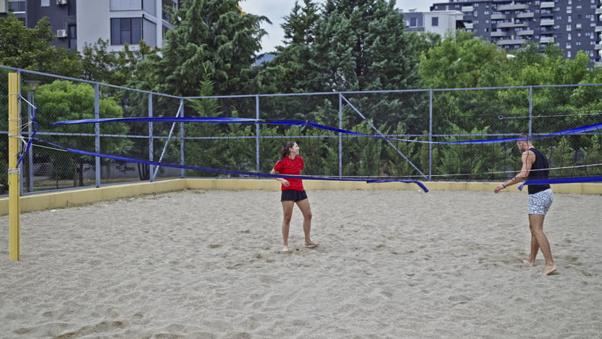 Two cheerful friends are captured playing an energetic game of beach volleyball on a sand court.
