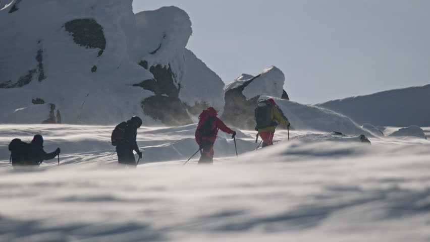 Determined mountaineers ascend snowy ridge amidst strong winds