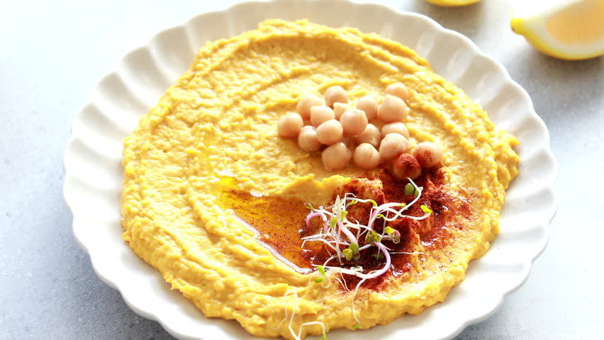 Hand dips bread into flavorful pumpkin hummus garnished with chickpeas and spices on a plate