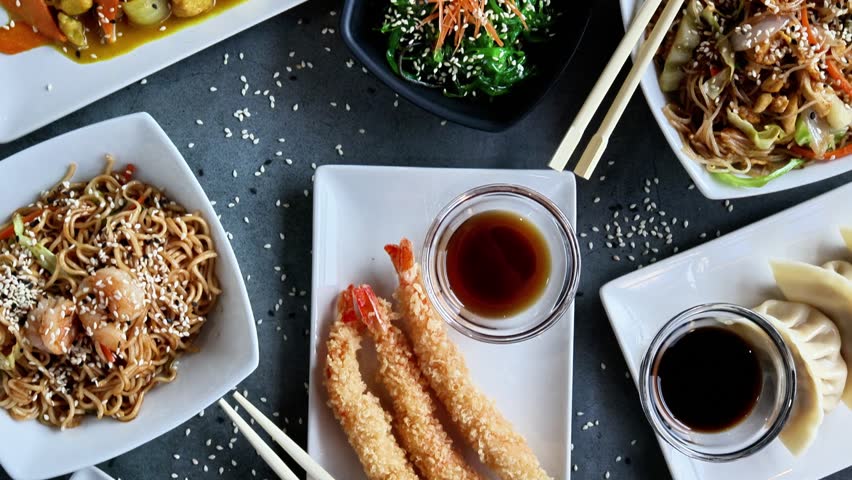Asian food dishes composition displaying variety of flavors, including tempura shrimps, noodles, and spring rolls
