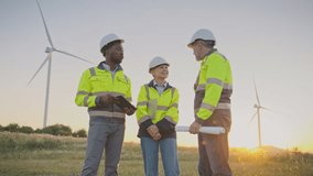 Male engineer shaking hands with his colleague. Wearing safety helmet and vest. Female supervisor standing with tablet in middle and smiling. Renewable energy field with wind turbines. - Powered by Shutterstock - Get 15% off with code: PIKWIZARD15