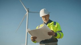 Male engineer in safety helmet and reflective jacket holding rolled blueprint looking into distance. Worker standing near wind turbine at field horizon during renewable energy inspection outside. - Powered by Shutterstock - Get 15% off with code: PIKWIZARD15
